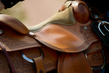 Close-up of a detailed leather horse saddle with tooling and silver conchos.