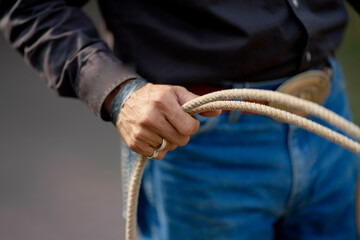 Close-up of a person's hands coiling a rope, dressed in jeans and a dark long-sleeved shirt, with a blurry background.
