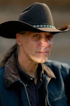 Cowboy wearing a black hat stares intently with a backdrop of subtle outdoor light.