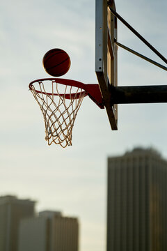 Basketball approaching the hoop against an early evening sky backdrop with city buildings in the distance.
