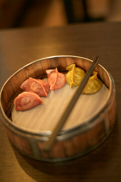 Dim sum in a bamboo steamer on a wooden table with chopsticks resting on top.