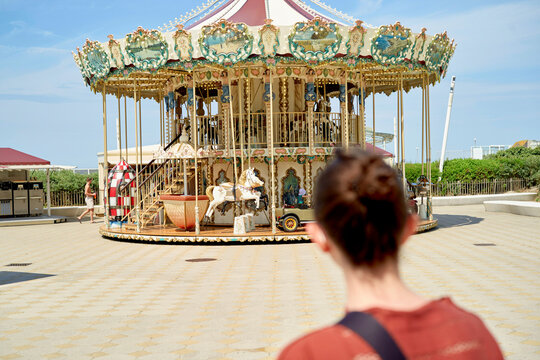 Young woman standing in front of an ornate carousel on a sunny day.