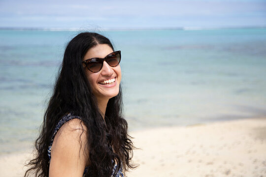 Woman in sunglasses smiling at the beach with clear skies and ocean in the background, Titikaveka, Rarotonga, Cook Islands