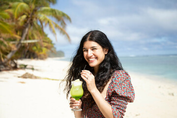 Smiling woman holding a green drink on a tropical beach with palm trees in the background, Titikaveka, Rarotonga, Cook Islands