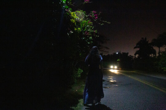 woman walking alone at night with oncoming vehicle headlights, Titikaveka, Rarotonga, Cook Islands