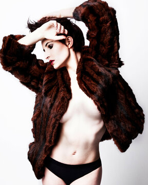Fashion model posing in a dark brown fur coat with a dramatic pose against a white background.