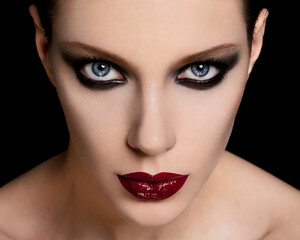 Close-up portrait of a woman with striking blue eyes and bold red lipstick on a black background.