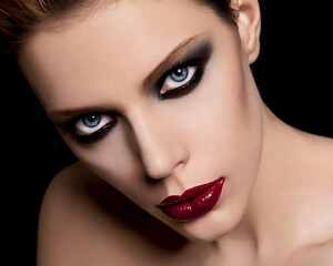Close-up portrait of a woman with dramatic red lipstick and smokey eye makeup against a black background.