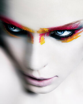 Close-up of a person with striking face paint in vibrant red and yellow tones, accentuating their eyes against pale skin.