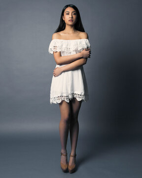 Elegant woman in a white off-the-shoulder dress standing against a gray background