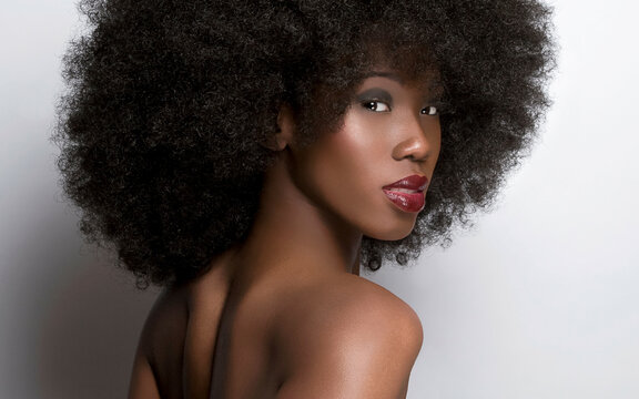 Close-up portrait of a woman with voluminous curly afro hair and striking makeup looking at the camera.