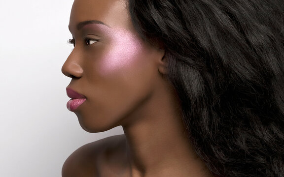 Close-up portrait of a woman with flawless skin and prominent cheekbones against a white background.