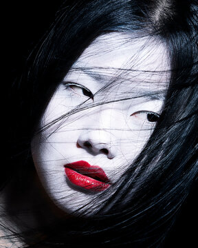 Close-up portrait of a woman with striking red lipstick and dark hair contrasting against her pale skin.