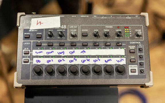 Audio mixing console with multiple adjustment knobs and channel inputs marked with handwritten labels.