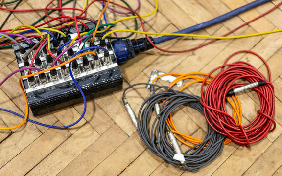 Audio cables and patch bay on a wooden floor in disarray.