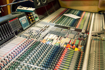 Close-up view of a professional sound mixing console with various knobs and sliders in a recording studio.