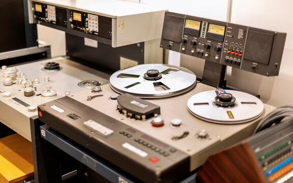 Vintage reel-to-reel tape recorder on a workbench with various control knobs, buttons, and VU meters.