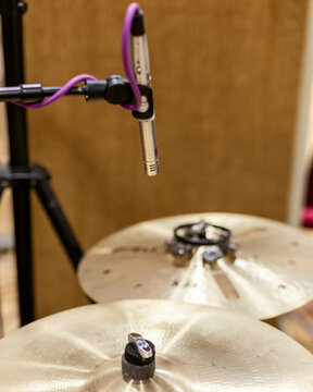 Close-up of a drum set with cymbals and a microphone stand in focus, set against a blurred warm background.