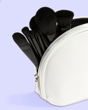 Close-up of a white makeup bag with various black brushes against a lavender background.