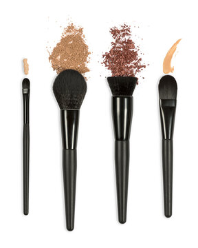 Makeup brushes and foundation, blush, and eyeshadow spills on a white background.
