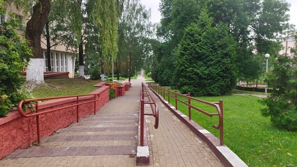 A stairway and inclined ramp with tiled floor and metal handrails was constructed to provide freedom of movement on the street for people with disabilities. Accessible environment. Nearby trees