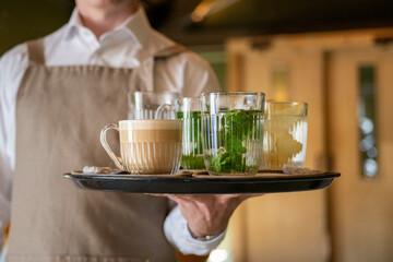 Waiter serving a tray of assorted beverages including coffee and refreshing drinks in glassware.