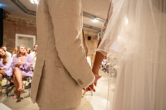 Wedding attendees seated as a man in a suit stands beside a sheer bridal veil, suggesting an ongoing wedding ceremony.