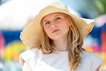 A young girl in a straw hat gazes thoughtfully ahead with colorful blurred background.