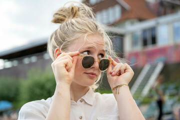 Young woman adjusting her sunglasses with a curious expression on her face.