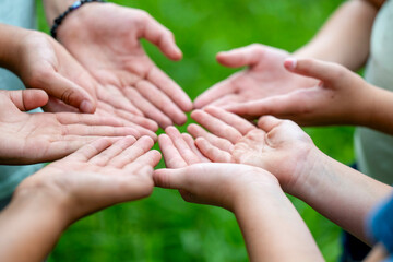 Open hands of several people extended towards each other against a green blurred background.