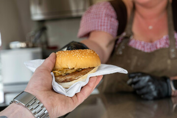 Hand receiving a freshly made burger from a server at a food stand.