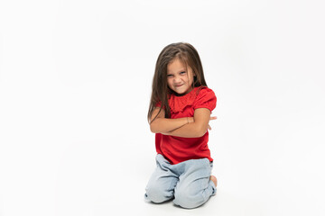 Full length imageof a  little girl is upset, but lying on the floor, looks into the room, holds her hands together, over white background.