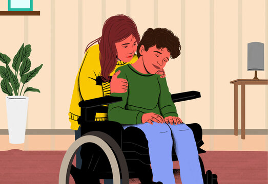 Woman in a yellow sweater comforting a man in a wheelchair inside a cozy room with a plant and paintings.