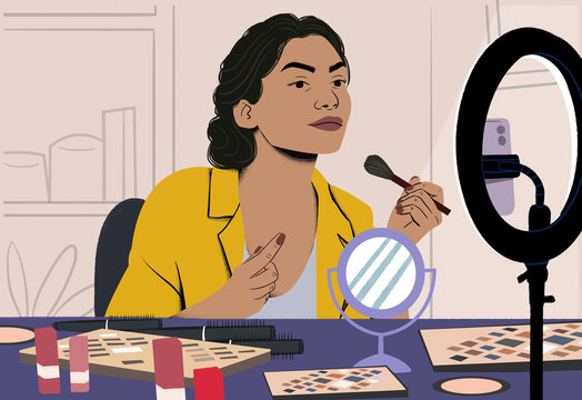 Woman applying makeup in front of a ring light and mirror with cosmetics on the table.