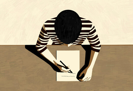 Person in a striped shirt intently writing on a piece of paper at a wooden table.