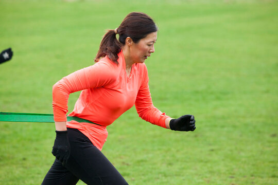 Athletic woman performs resistance band training on a grassy field.