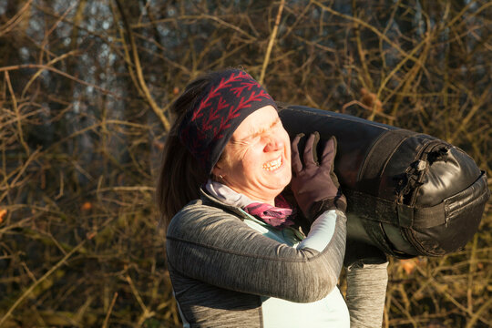 Woman grimacing as she carries a heavy tire on her shoulder during an outdoor workout