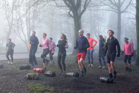 Group of adults engaging in an outdoor exercise bootcamp amidst foggy conditions, displaying teamwork and physical fitness.