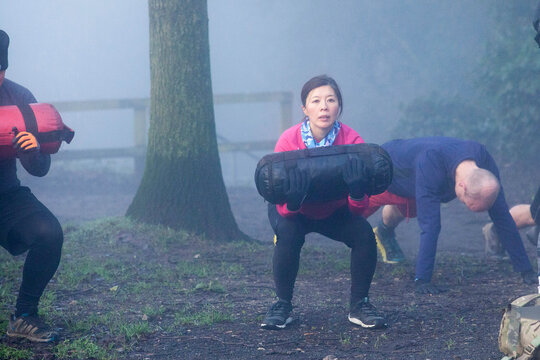 Group of people exercising with weights in a foggy outdoor setting.