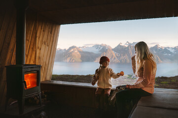 Family mother and child relaxing in cozy mountain hut with fireplace and panoramic window with...