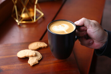 Hot Cappuccino coffee with black cup on old wooden table with isolate in black background