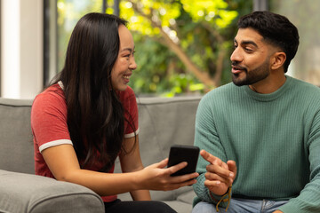 Diverse friends sitting on couch, talking and using smartphone, enjoying conversation