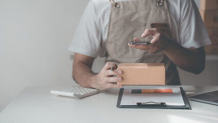 Fototapeta premium Male SME owner, entrepreneur, works boxes and checks online orders. To prepare to pack boxes to sell to customers, online SME business ideas Close-up pictures