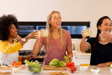 Friends in kitchen toasting with drinks, preparing fresh vegetables for meal