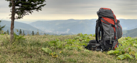 Tourist adventure backpack, packed hiking travel backpack stands on high hill against backdrop of mountains. Filled tourist hiking backpack that stands on the grass. Camping and trekking equipment