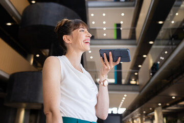 Smiling businesswoman using smartphone for voice message in modern office building