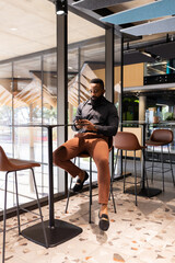 Using smartphone, businessman sitting at high table in modern office space