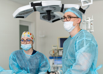 Surgeons in a modern operating room. A surgeon and an assistant are engaged in a surgical procedure, wearing scrubs and masks in a bright operating room.