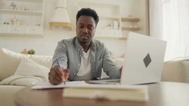 African American male student learning online, doing homework with laptop. Portrait of black man using computer in living room, workplace for online job from home, user shopping online in website