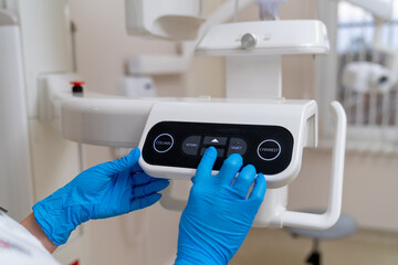 Dental pro using X-ray machine indoors. A dental professional in blue gloves adjusts the controls of a dental X-ray machine in a bright clinic setting.